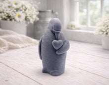 Load image into Gallery viewer, A 3D handmade vegan soap sculpted as a standing penguin tenderly cradling a heart against its chest, displayed on a light wooden surface in a bright farmhouse setting.