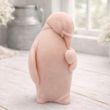 Load image into Gallery viewer, A 3D handmade vegan soap sculpted as a standing penguin tenderly cradling a heart against its chest, displayed on a light wooden surface in a bright farmhouse setting.