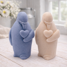Load image into Gallery viewer, A 3D handmade vegan soap sculpted as a standing penguin tenderly cradling a heart against its chest, displayed on a light wooden surface in a bright farmhouse setting.
