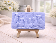 Load image into Gallery viewer, A rectangular handmade vegan soap bar gift, featuring a detailed relief carving of several dogs and a cat sitting together, with the words "all paws matter" and two paw prints embossed at the top, displayed on a wooden easel. Made in Blackpool.