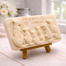 Load image into Gallery viewer, A rectangular handmade vegan soap bar gift, featuring a detailed relief carving of several dogs and a cat sitting together, with the words "all paws matter" and two paw prints embossed at the top, displayed on a wooden easel. Made in Blackpool.
