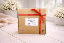 Load image into Gallery viewer, Kraft paper gift box with red ribbon and 'Laughing Pigs' label on a wooden surface.