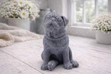 Load image into Gallery viewer, A detailed handmade vegan soap sculpted in the shape of a sitting pug dog with characteristic facial wrinkles and a tilted head, in a natural tone, displayed on a light wooden surface.