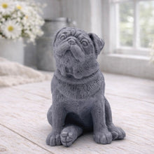 Load image into Gallery viewer, A detailed handmade vegan soap sculpted in the shape of a sitting pug dog with characteristic facial wrinkles and a tilted head, in a natural tone, displayed on a light wooden surface.