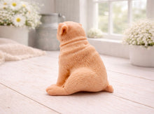 Load image into Gallery viewer, A detailed handmade vegan soap sculpted in the shape of a sitting pug dog with characteristic facial wrinkles and a tilted head, in a charcoal-grey tone, displayed on a light wooden surface.