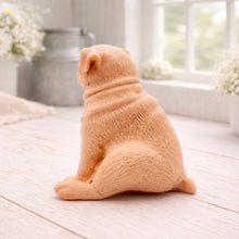 Load image into Gallery viewer, A detailed handmade vegan soap sculpted in the shape of a sitting pug dog with characteristic facial wrinkles and a tilted head, in a charcoal-grey tone, displayed on a light wooden surface.