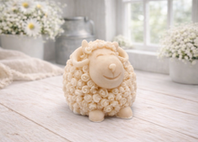 Load image into Gallery viewer, A highly detailed handmade vegan soap sculpted in the shape of a sturdy ram with a thick coat of tight, curly wool and large, elegant curved horns, displayed on a light wooden surface in a bright farmhouse setting.