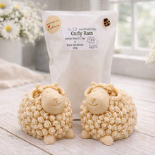 Load image into Gallery viewer, A highly detailed handmade vegan soap sculpted in the shape of a sturdy ram with a thick coat of tight, curly wool and large, elegant curved horns, displayed on a light wooden surface in a bright farmhouse setting.