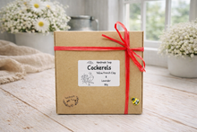 Load image into Gallery viewer, Box of handmade soap with a red ribbon on a wooden surface with flowers in the background
