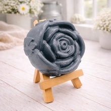 Load image into Gallery viewer, A handmade vegan soap, intricately sculpted in the shape of a large, blooming rose flower with layered petals, displayed on a small wooden easel against a bright win
