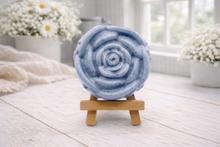 Load image into Gallery viewer, A handmade vegan soap, intricately sculpted in the shape of a large, blooming rose flower with layered petals, displayed on a small wooden easel against a bright win