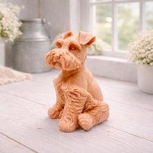 Load image into Gallery viewer, A detailed handmade vegan soap sculpted in the shape of a sitting Schnauzer dog with characteristic fluffy eyebrows and beard, in a natural colour, set against a bright window and white flowers. By soap Simple creations