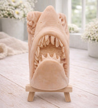 Load image into Gallery viewer, A 3D handmade vegan soap sculpted into a realistic great white shark head with its jaws wide open to reveal multiple rows of sharp teeth, displayed on a miniature wooden easel in a bright farmhouse setting.