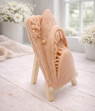 Load image into Gallery viewer, A 3D handmade vegan soap sculpted into a realistic great white shark head with its jaws wide open to reveal multiple rows of sharp teeth, displayed on a miniature wooden easel in a bright farmhouse setting.