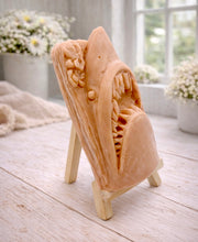 Load image into Gallery viewer, A 3D handmade vegan soap sculpted into a realistic great white shark head with its jaws wide open to reveal multiple rows of sharp teeth, displayed on a miniature wooden easel in a bright farmhouse setting.