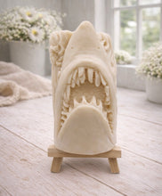 Load image into Gallery viewer, A 3D handmade vegan soap sculpted into a realistic great white shark head with its jaws wide open to reveal multiple rows of sharp teeth, displayed on a miniature wooden easel in a bright farmhouse setting.