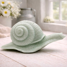 Load image into Gallery viewer, A highly detailed handmade vegan soap in a slate-grey tone, sculpted in the shape of a realistic snail with a prominent spiralled shell and a textured, leathery body, displayed on a light wooden surface.