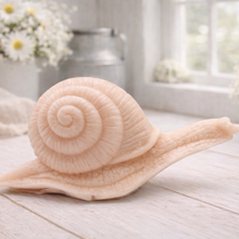Load image into Gallery viewer, A highly detailed handmade vegan soap in a slate-grey tone, sculpted in the shape of a realistic snail with a prominent spiralled shell and a textured, leathery body, displayed on a light wooden surface.