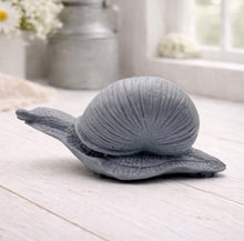 Load image into Gallery viewer, A highly detailed handmade vegan soap gift, sculpted in the shape of a realistic snail with a prominent spiralled shell and a textured, leathery body, displayed on a light wooden surface. Handmade in Blackpool.
