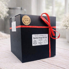 Load image into Gallery viewer, Black gift box with red ribbon and 'Spooky Soap Gift Set' label on a light wooden surface.