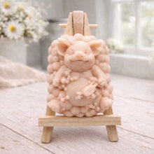 Load image into Gallery viewer, A detailed handmade vegan soap, sculpted as a cheerful pig sitting in a mound of bubbles and holding a scrubbing brush, displayed on a miniature wooden easel against a soft farmhouse window background