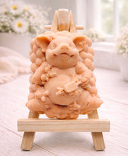 Load image into Gallery viewer, A detailed handmade vegan soap in a natural cream tone, sculpted as a cheerful pig sitting in a mound of bubbles and holding a scrubbing brush, displayed on a miniature wooden easel against a soft farmhouse window background.