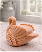 Load image into Gallery viewer, handmade vegan soap, sculpted into the shape of a graceful swan with detailed feathering on its wings and a curved neck, displayed on a light wooden surface in a bright farmhouse setting.
