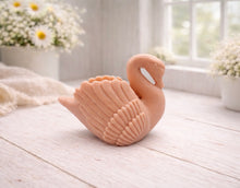 Load image into Gallery viewer, A 3D handmade vegan soap, sculpted into the shape of a graceful swan with detailed feathering on its wings and a curved neck, displayed on a light wooden surface in a bright farmhouse setting.