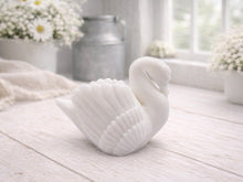 Load image into Gallery viewer, A 3D handmade vegan soap, sculpted into the shape of a graceful swan with detailed feathering on its wings and a curved neck, displayed on a light wooden surface in a bright farmhouse setting.