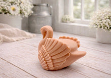 Load image into Gallery viewer, A 3D handmade vegan soap, sculpted into the shape of a graceful swan with detailed feathering on its wings and a curved neck, displayed on a light wooden surface in a bright farmhouse setting.