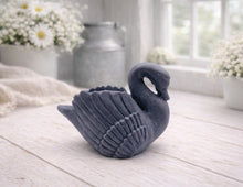 Load image into Gallery viewer, A 3D handmade vegan soap, sculpted into the shape of a graceful swan with detailed feathering on its wings and a curved neck, displayed on a light wooden surface in a bright farmhouse setting.