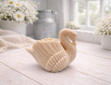 Load image into Gallery viewer, A 3D handmade vegan soap, sculpted into the shape of a graceful swan with detailed feathering on its wings and a curved neck, displayed on a light wooden surface in a bright farmhouse setting.