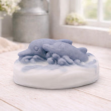 Load image into Gallery viewer, A handmade vegan soap featuring two grey dolphins jumping through white frothy waves; the base is white, and the dolphins are highly detailed, displayed on a light wooden surface against a soft farmhouse background.