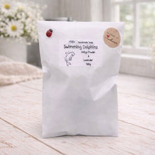 Load image into Gallery viewer, White bag labeled 'Swimming Dolphins' on a wooden surface with flowers in the background