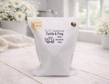 Load image into Gallery viewer, White bag of handmade soap labeled 'Turtle & Frog' on a light wooden surface with flowers in the background.