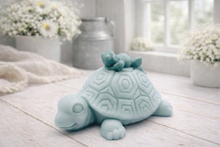 Load image into Gallery viewer, A handmade vegan soap in a soft mint green tone, sculpted into a large friendly turtle with a geometric shell pattern and a small, cute frog sleeping peacefully on its back.