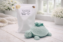Load image into Gallery viewer, Teal turtle-shaped soap and white bag with branding on a light wooden surface.