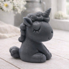 Load image into Gallery viewer, A 3D handmade vegan soap sculpted into a cute sitting unicorn with a spiralled horn, a smiling expression with a closed winking eye, and a bubbly mane and tail, displayed on a light wooden surface in a bright farmhouse setting.