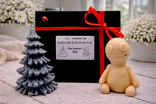 Load image into Gallery viewer, A handmade vegan soap gift set featuring a cream-coloured voodoo doll soap with stitched details and a grey tiered Christmas tree soap, presented in a black gift box tied with a red raffia ribbon and a small ladybird embellishment.