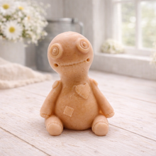 Load image into Gallery viewer, A handmade vegan soap gift in the shape of a stitched voodoo doll with button eyes and a small patch on its chest, sitting on a light wooden surface.