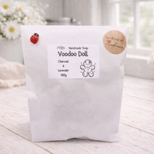 Load image into Gallery viewer, Handmade soap package labeled 'Voodoo Doll' on a wooden surface with flowers in the background.