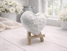 Load image into Gallery viewer, A pair of handmade vegan soaps shaped like hearts and displayed on miniature wooden easels; one heart is textured like a grey tuxedo with a bow tie and buttons, and the other is a white bridal gown heart with intricate lace patterns and a pearl necklace detail.