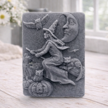 Load image into Gallery viewer, handmade vegan soap bar featuring a detailed relief carving of a witch flying on a broomstick past a crescent moon, owls, and pumpkins.
