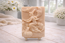 Load image into Gallery viewer, handmade vegan soap bar featuring a detailed relief carving of a witch flying on a broomstick past a crescent moon, owls, and pumpkins.