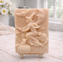 Load image into Gallery viewer, handmade vegan soap bar featuring a detailed relief carving of a witch flying on a broomstick past a crescent moon, owls, and pumpkins.