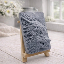 Load image into Gallery viewer, A rectangular handmade vegan soap featuring a highly detailed, 3D relief carving of a wolf's head in profile with a thick, textured mane, displayed on a miniature wooden easel.