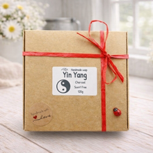 Load image into Gallery viewer, Gift box with a red ribbon and 'Yin Yang' label on a wooden surface with flowers in the background
