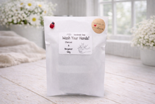 Load image into Gallery viewer, White bag labeled 'Wash Your Hands!' with decorative elements on a light wooden surface.