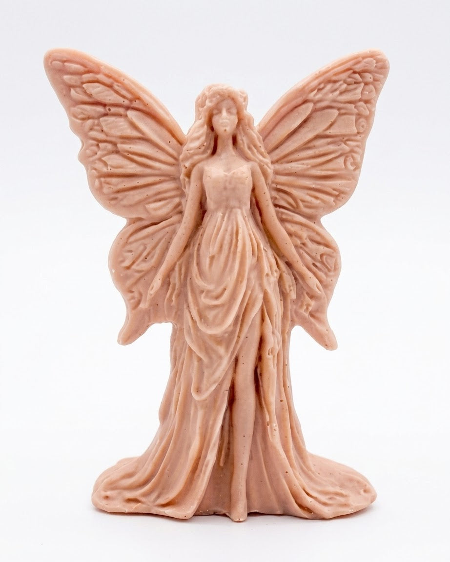 A detailed handmade vegan soap featuring an elegant fairy with large, intricate butterfly-style wings, a flowing gown, and long hair, standing against a bright farmhouse window background.