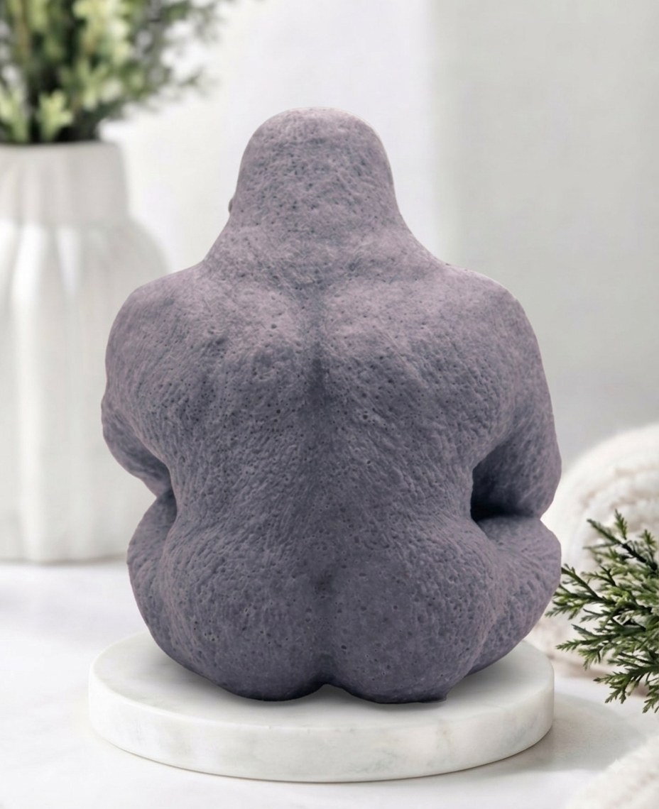 A large gray gorilla handmade soap sitting on a white marble base, photographed in a softly styled indoor setting with blurred decor in the background.